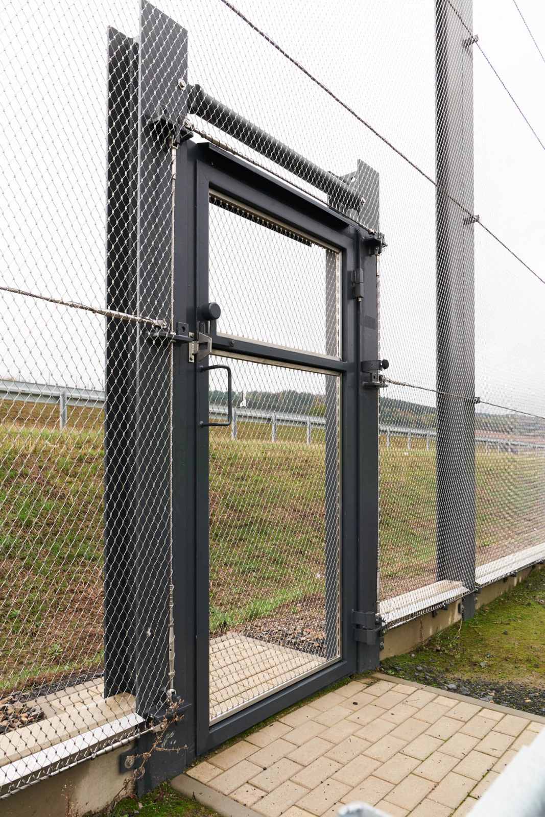 A door inside a stainless steel net fence by Jakob Rope Systems