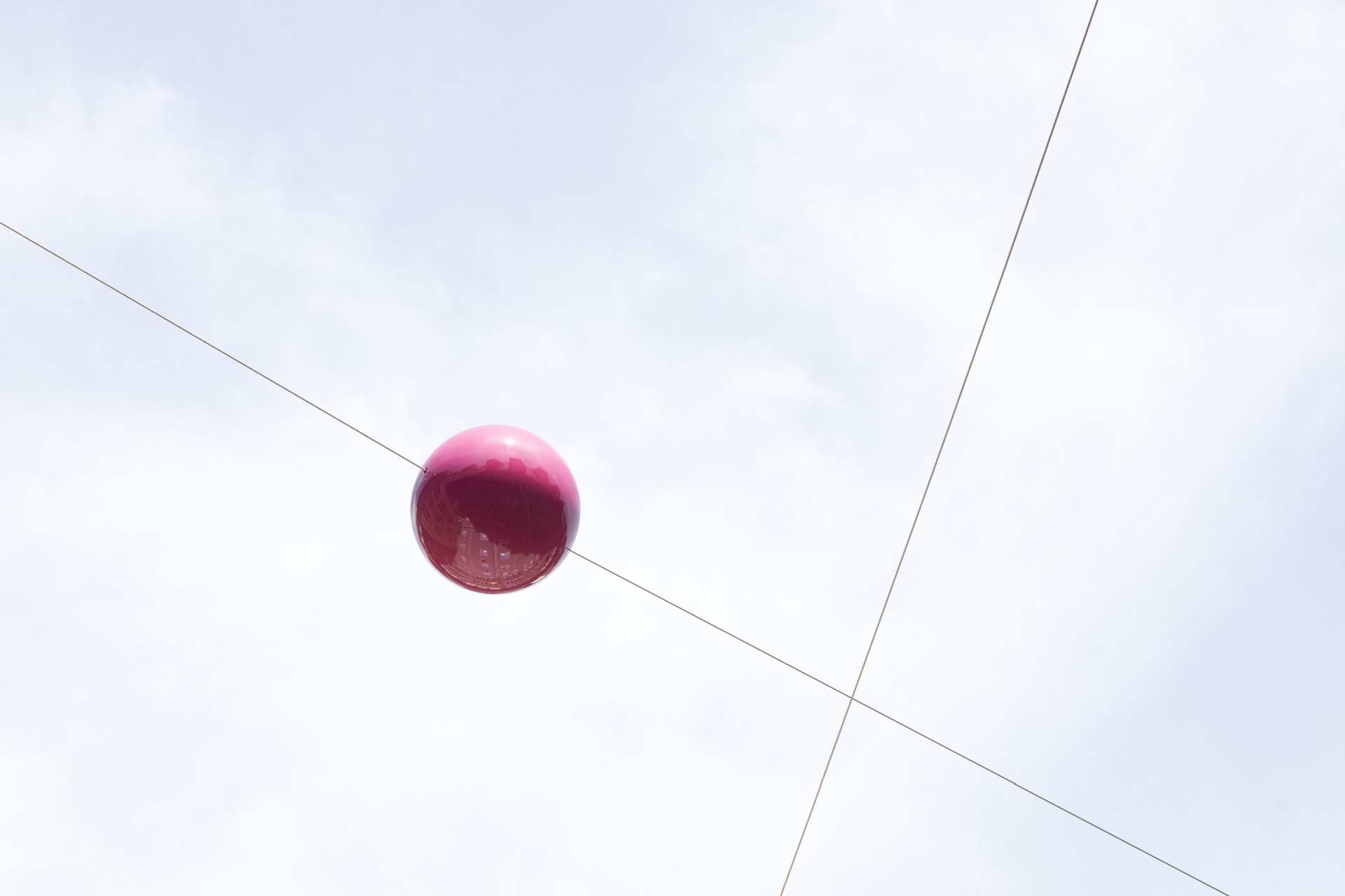 The red plastic ball against the sky with intersecting steel cables