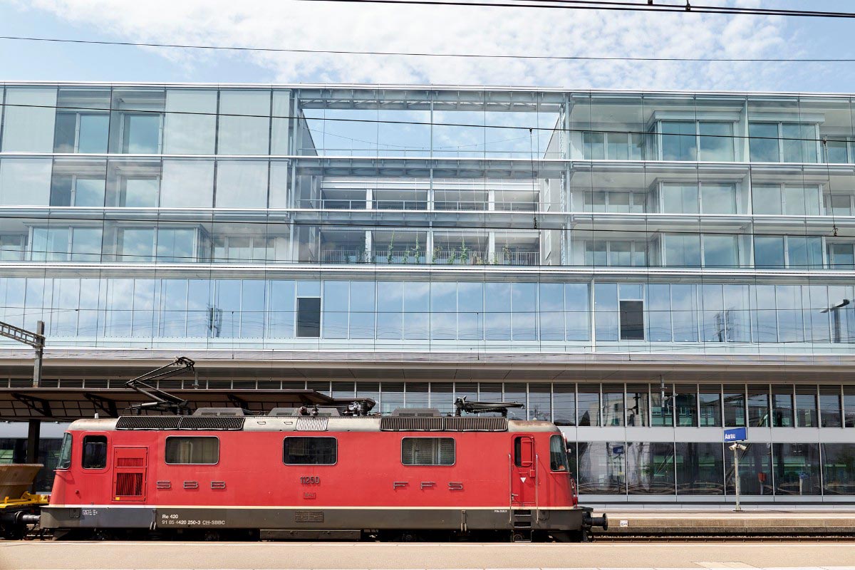 A locomotive stands in Aarau station before a modern office building with interior greening by Jakob Rope Systems