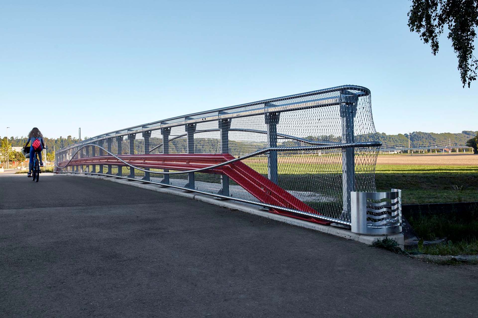 Webnet covers the railings on both sides of the bridge. It serves not only as a railing infill, but lets the striking red crash barriers and the curved steel railings shine.