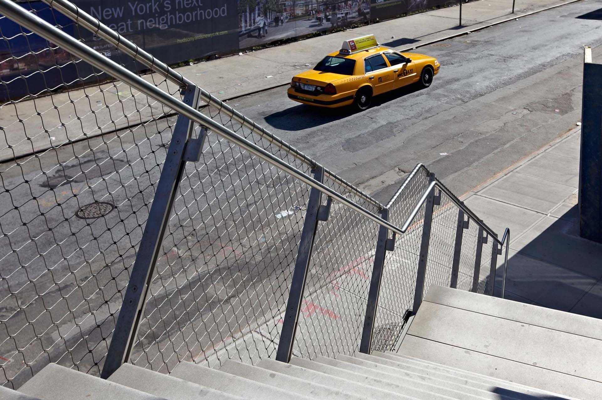 A yellow New York cab in front of a stair with a Webnet railing